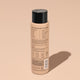 A bottle of Odele Thickening Conditioner stands upright against a plain, light orange backdrop with the back of the label facing the camera.