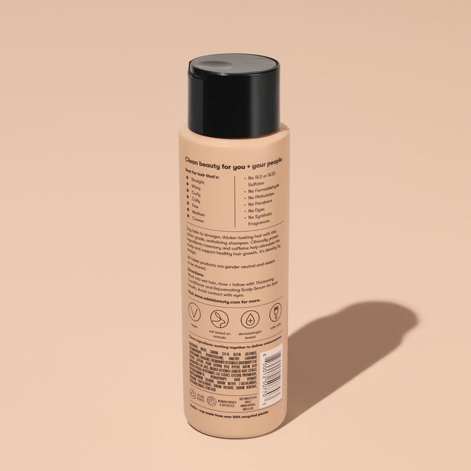 A bottle of Odele Thickening Shampoo stands upright against a plain, light orange backdrop with the back of the label facing the camera.