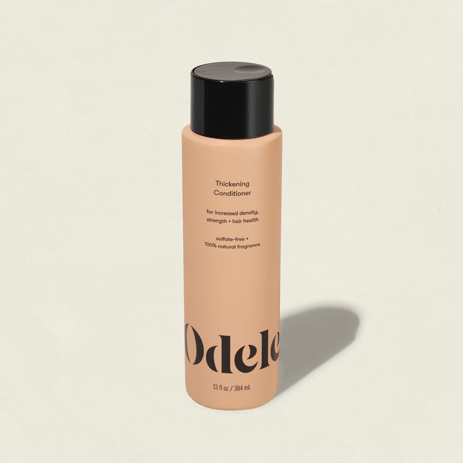 A peach-colored bottle of Odele Thickening Conditioner with a black cap stands upright on a plain background. The label promotes hair strength, density, and addresses thinning hair.