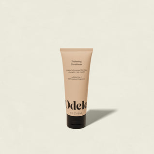 A beige tube of Odele Thickening Conditioner Mini (2 fl oz/59 mL) stands upright on a light background, with a label highlighting benefits for thinning hair: improved density, strength, and overall hair health.