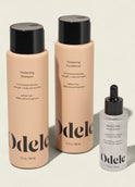 The Odele Thickening Set includes thickening shampoo and conditioner in tall beige bottles with black caps, plus a rejuvenating scalp serum in a small clear bottle with a black dropper cap.