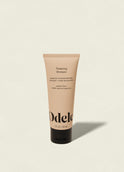 A beige tube of Odele Thickening Shampoo Mini stands upright on a light background, featuring bold black text and a sleek black cap, highlighting its revitalizing formula designed to promote healthy hair growth.