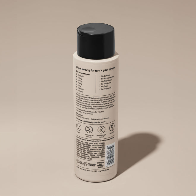 A bottle of Odele Ultra Sensitive Shampoo stands upright against a plain, light-colored backdrop with the back of the label facing the camera.
