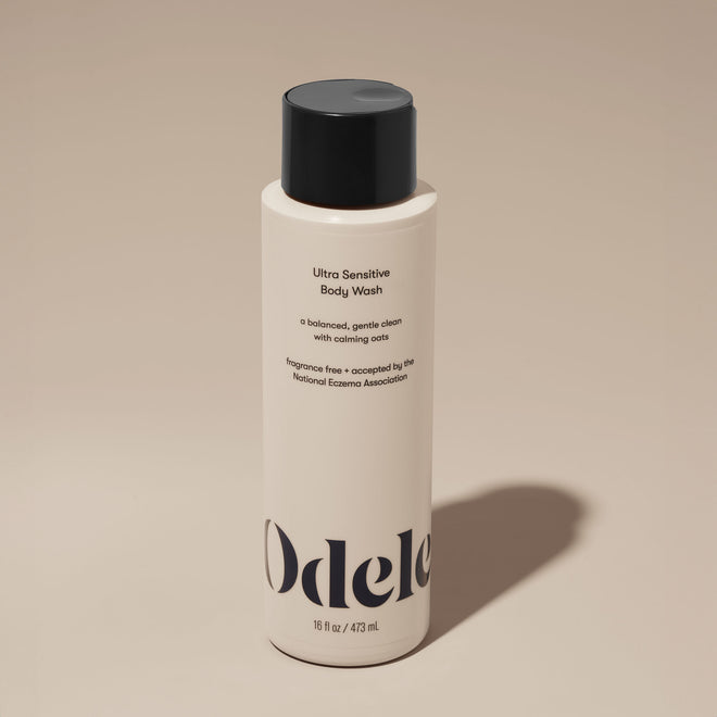 A bottle of Odele Ultra Sensitive Body Wash stands upright against a plain, light-colored backdrop with the front of the label facing the camera.