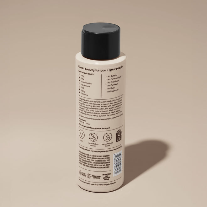 A bottle of Odele Ultra Sensitive Body Wash stands upright against a plain, light-colored backdrop with the back of the label facing the camera.