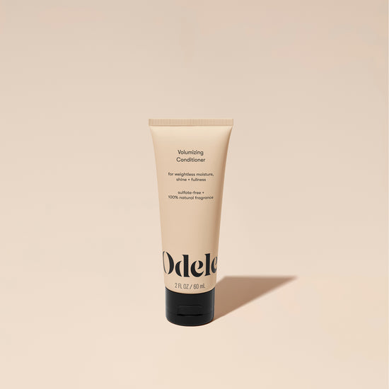 A tube of Odele Volumizing Conditioner stands upright against a plain, light orange backdrop with the front of the label facing the camera.