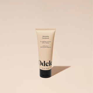 A tube of Odele Volumizing Conditioner stands upright against a plain, light orange backdrop with the front of the label facing the camera.