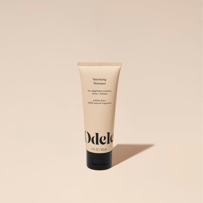A tube of Odele Volumizing Shampoo stands upright against a plain, light orange backdrop with the front of the label facing the camera.