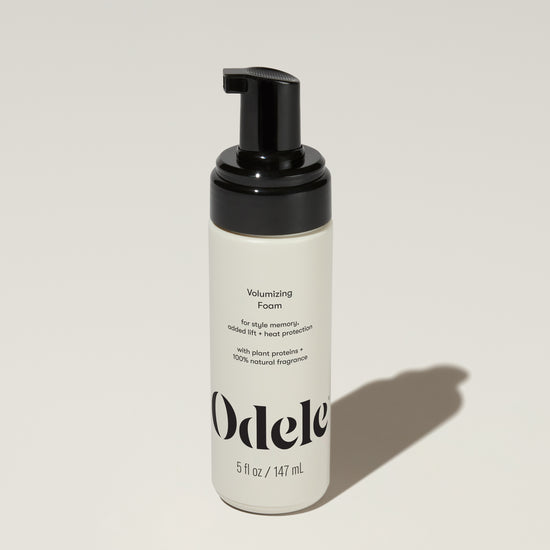 A bottle of Odele Volumizing Foam stands upright against a plain light-colored backdrop with the front of the label facing the camera.