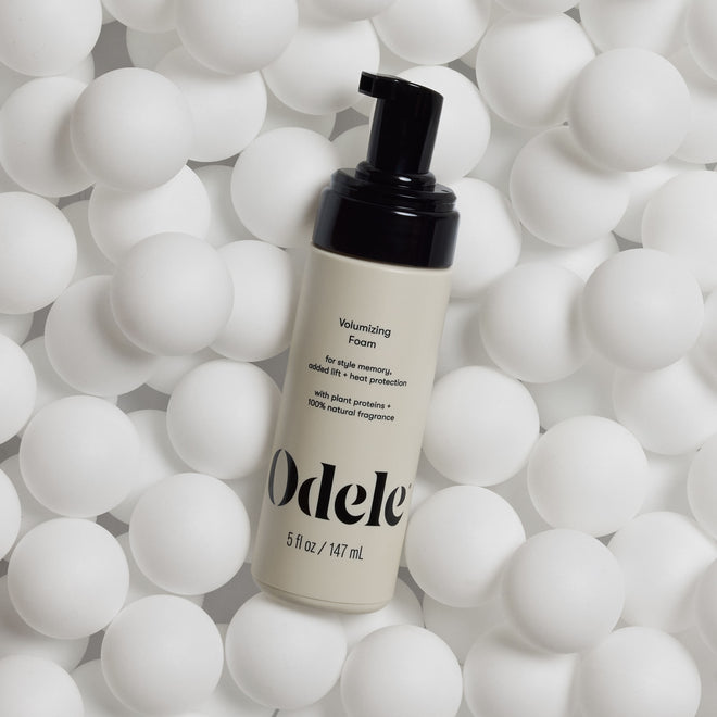A bottle of Odele Volumizing Foam sits on a bed of white ping pong balls.