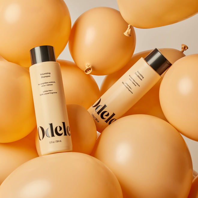 Bottles of Odele Volumizing Shampoo and Conditioner are surrounded by orange balloons against a neutral background.