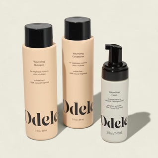 The Odele Volumizing Set, featuring minimalist beige and gray bottles with black text and handy pump dispensers, stands upright on a light surface.