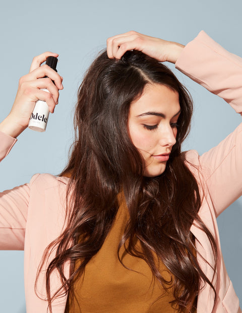 woman with long dark hair applying dry shampoo to scalp